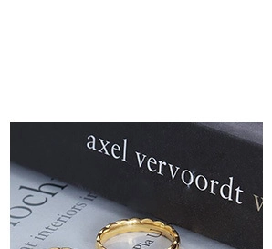 Close-up of polished 18K gold-plated wavy scallop ring on artistic book background
