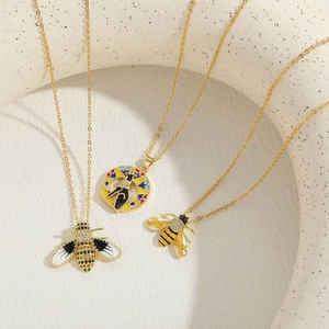 Three gold bee necklaces with enamel dripping and zircon accents on a ceramic stand