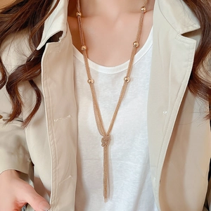 Detail of layered gold chain necklace with knot and tassels on a model wearing a beige coat