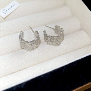 Macro detail of silver C-shaped earrings with irregular crumpled texture on velvet tray