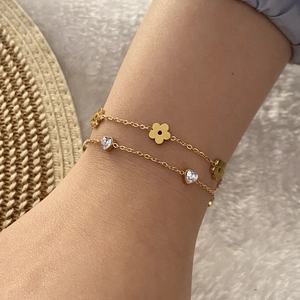 Double-layer gold bracelet with heart zircon and flower pendants on a model's wrist