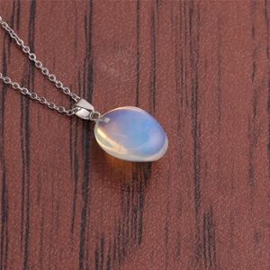 Macro view of oval white opal pendant on a silver metal chain over dark wood background
