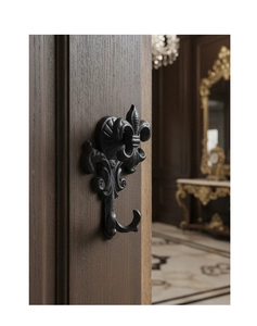 Close-up of vintage black cast iron fleur-de-lis hook mounted on dark wood background