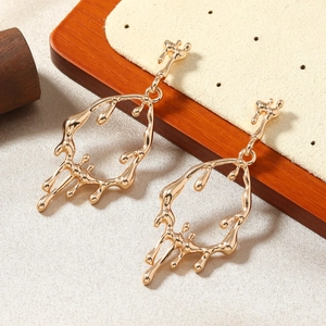 Macro shot of liquid metal drop earrings in gold finish on natural wooden background