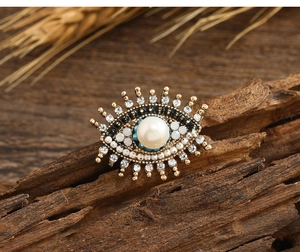 Macro detail of retro evil eye brooch with freshwater pearl and crystals on wood