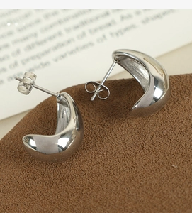 Macro shot of silver polished C-shaped chunky hollow earrings on a brown display