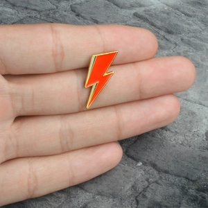Creative red lightning bolt enamel pin with gold metal edges held in hand for scale