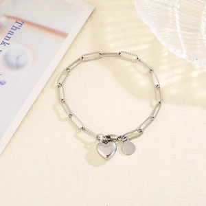 Close-up of silver paperclip chain bracelet with heart and circular metal charms