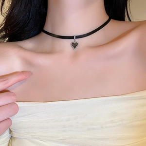 Detail of a black velvet choker featuring a delicate heart pendant on a model's neck