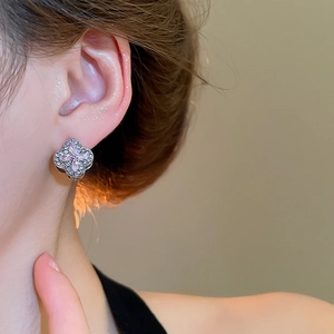 Detailed close-up of a silver four-leaf clover earring with pink crystals on an ear