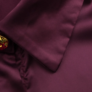Macro detail of purple satin fabric texture with a premium gold button on the collar