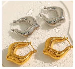 Detailed macro view of gold and silver chunky teardrop earrings on water-beaded surface