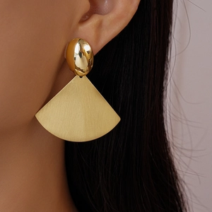 Macro close-up of geometric fan-shaped earrings with brushed and polished gold finishes