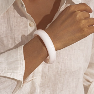 Close-up of minimalist white resin round bangle worn over white linen shirt sleeve