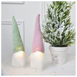 Close-up of glowing Christmas gnomes with knit hats and warm LED lights on table