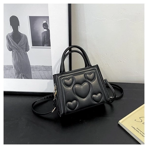 Détail d'un sac bandoulière en cuir noir avec motif cœur en 3D dans un décor professionnel