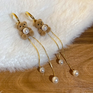 Close-up of brown flocked bear earrings with pearl detail and long golden tassels