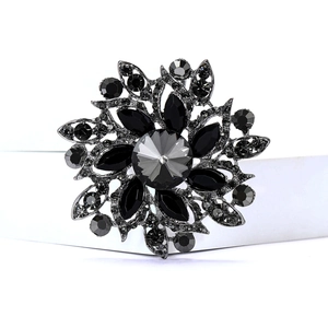 Close-up of black flower brooch with dark rhinestones and crystal petals on white surface