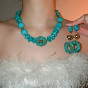 Detail view of teal acrylic bead necklace and earring set on model with feather outfit
