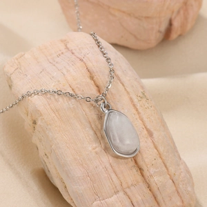Macro detail of silver-tone teardrop pendant with moonstone-like gem on beige rock