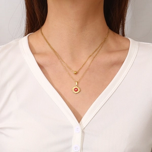 Double-layered gold stainless steel necklace with red evil eye pendant worn by model