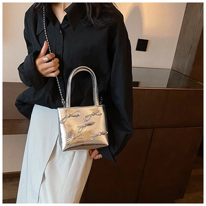 Silver metallic shoulder bag with decorative bows and chain strap in a lifestyle setting