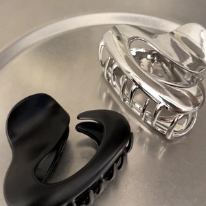 Close-up of irregular hair claws in silver metal and matte black on a steel tray