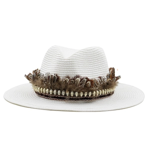 Close-up of white woven straw fedora hat featuring brown feather and gold skull chain