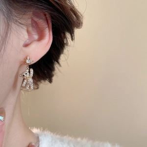 Detail of gold teddy bear earrings with star stud and zircon stones on a model ear