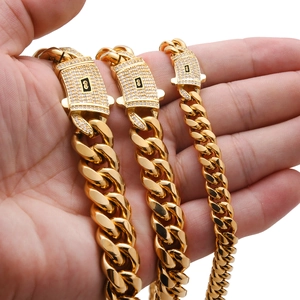 Detailed close-up of golden Cuban links with iced-out S-logo clasp held in hand
