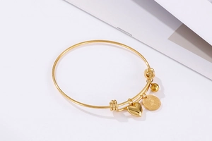 Close-up of golden stainless steel heart and coin charms on an expandable bangle