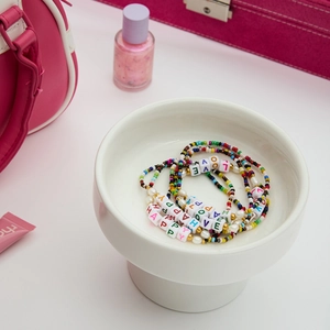 Close-up of colorful beaded bracelets with HAPPY and LOVE charms in a ceramic bowl