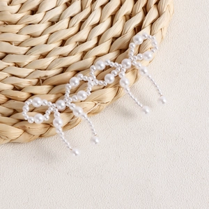 Detail of handmade woven pearl bow earring with elegant trailing tassels for women