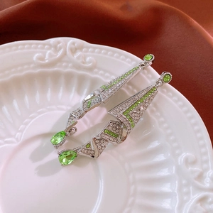Detail of silver drop earrings with green waterdrop crystals on a white ceramic plate