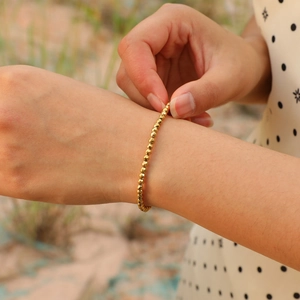Macro detail of gold-plated faceted beads on a slim bracelet worn on a female wrist