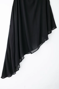 Détail d'une robe en mousseline noire avec un ourlet asymétrique élégant sur mur blanc