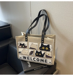 Detail of beige canvas tote bag with cartoon cat prints and black faux leather handles