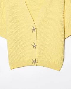 Détail d'un cardigan jaune en maille avec trois boutons décoratifs en forme d'étoile