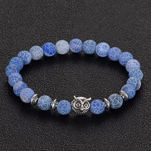 Close-up of blue crackle bead bracelet featuring a silver owl charm on dark texture