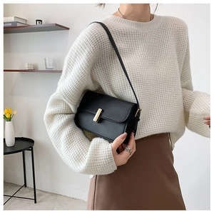 Detail of minimalist black leather saddle bag with gold buckle and adjustable shoulder strap