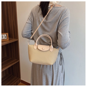 Detail of light beige woven crossbody bag with leather flap and button closure on model