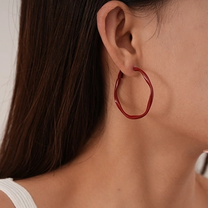 Detail view of a model wearing dark red twisted geometric hoop earrings in a modern style