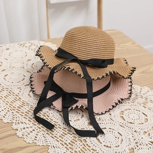 Detail of woven straw sun hats featuring black bow ribbons and delicate lace scalloped edges