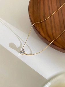 Detailed close-up of a heart-shaped zircon pendant with a thin gold chain on wood