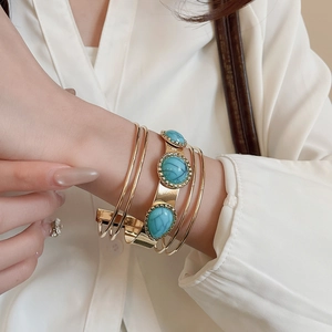 Detail of gold multilayer open cuff bracelet featuring three oval turquoise stones on a wide band
