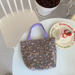 Close-up of floral corduroy tote bag with purple straps and snap button on a cafe table