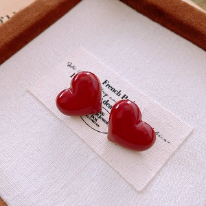 Detailed view of glossy red heart stud earrings on a textured paper background