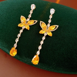 Detailed shot of gold long earrings with yellow teardrop zircon and butterfly shape on velvet