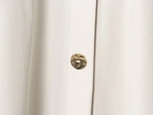 Detail of a textured cream woven fabric featuring a unique golden metal button closure