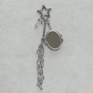 Detail of silver star-shaped clasp with oval mirror and long chain tassels on a keychain